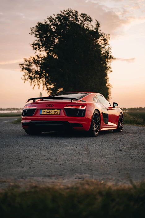 A sleek, shiny red car parked on a country road at sunset