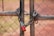 A metal chain-link fence is secured by a heavy chain and a red padlock. The focus is on the closed lock and intertwined chain, signifying security or restriction. The background is out of focus, with reddish-brown earth tones.