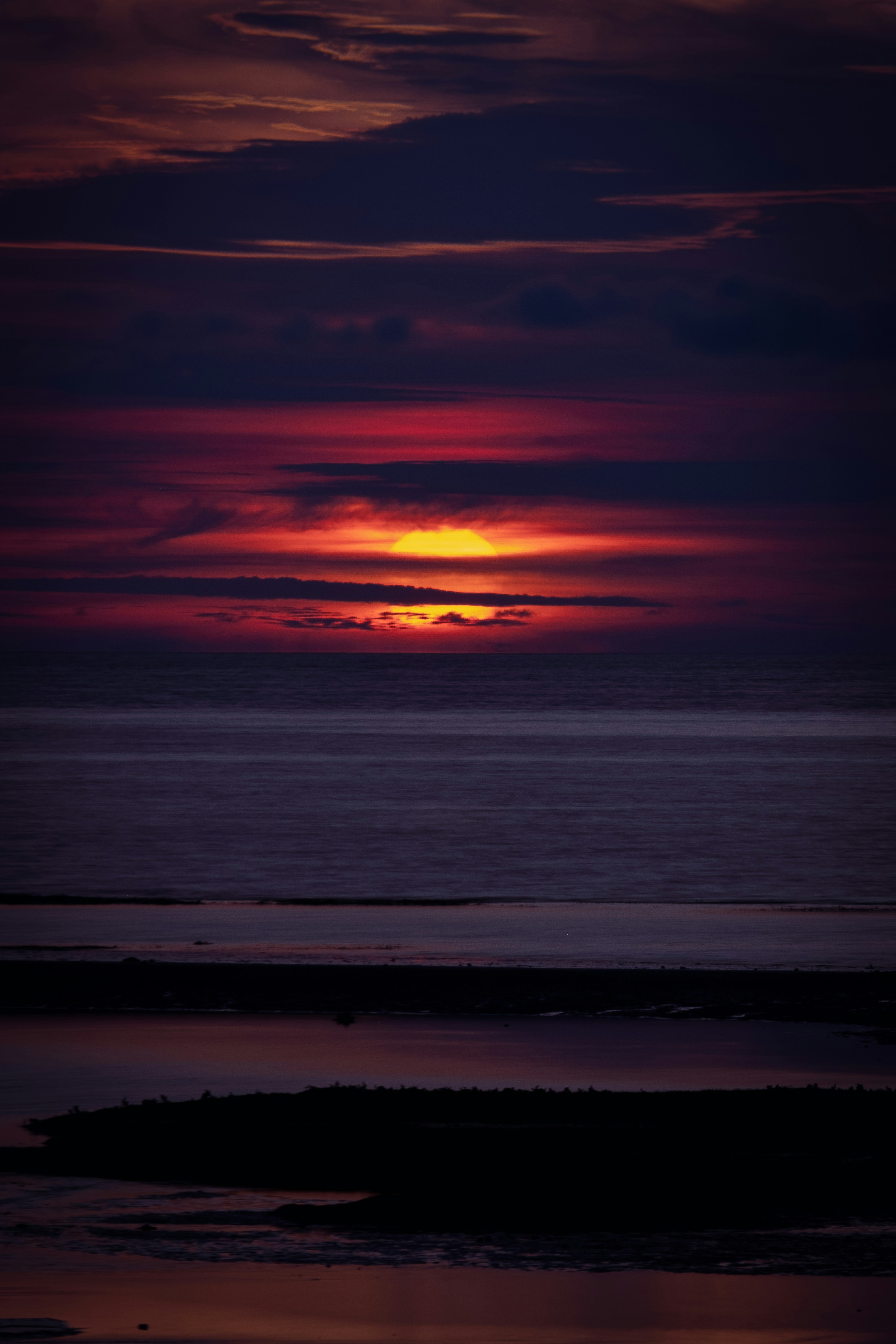 the sun is setting over the ocean with a boat in the water