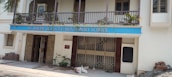 A building facade with a blue sign reading 'St. Joseph of Cluny Montessori School.' The balcony features potted plants and the entrance includes two metal gates. A green bicycle is parked near the entrance, with bricks and construction materials stacked on the side.