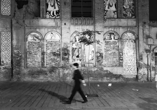 A monochrome street scene showing a lone figure walking past textured urban walls, embodying the essence of city life.