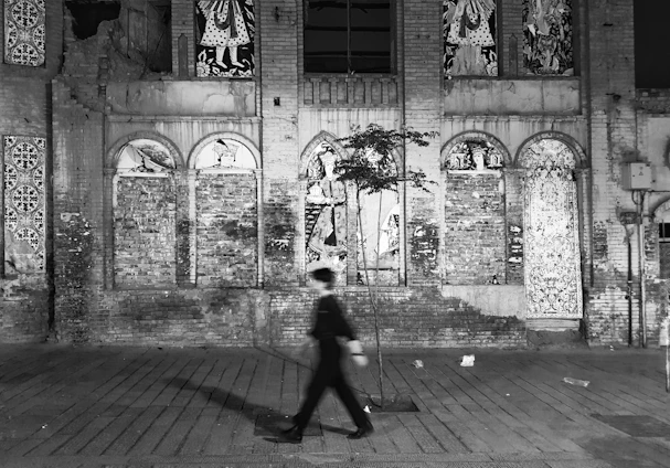 A monochrome street scene showing a lone figure walking past textured urban walls, embodying the essence of city life.