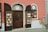 A storefront with a glass door and two display cabinets filled with jewelry and decorative items. The building has a warm pink and cream exterior with a brown door and shutters. The displays feature various jewelry pieces, likely made of crystal or glass, placed on white stands.