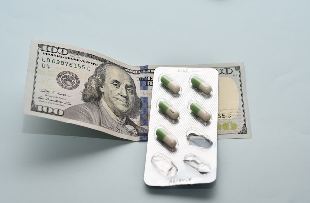 a pack of pills sitting on top of a hundred dollar bill