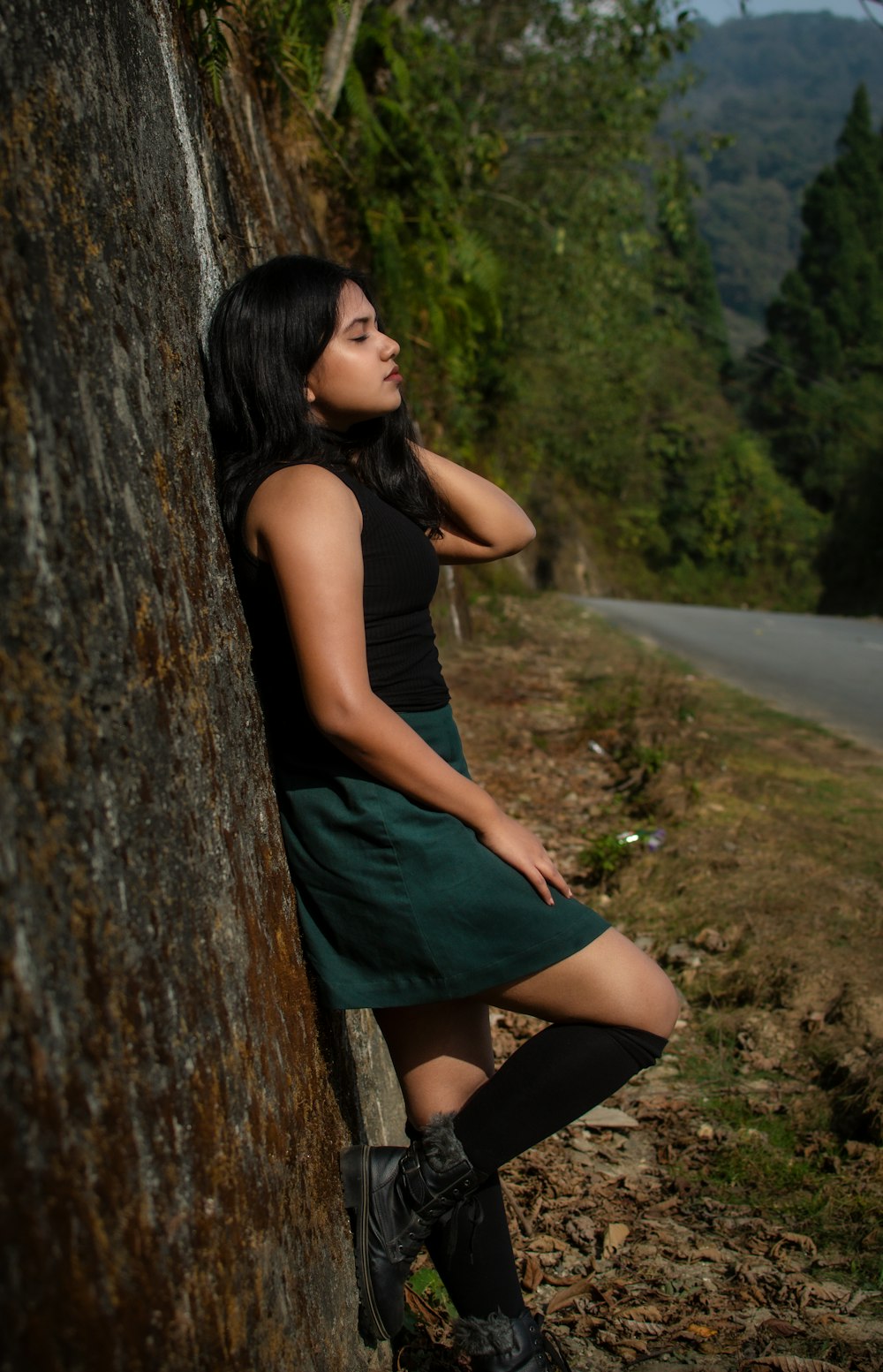 a woman leaning against a tree on the side of a road