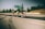 Three cyclists ride swiftly along a highway with blurred motion indicating speed. They are in a competitive stance, wearing helmets and athletic gear. There are road signs and trees in the background.