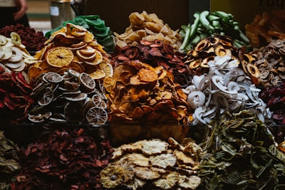 A variety of dried fruits are displayed in an arrangement, with distinct piles showcasing vibrant colors and textures. The assortment includes slices of oranges, apples, limes, and coconut, among others. The rich, organic hues create a visually appealing, rustic theme.