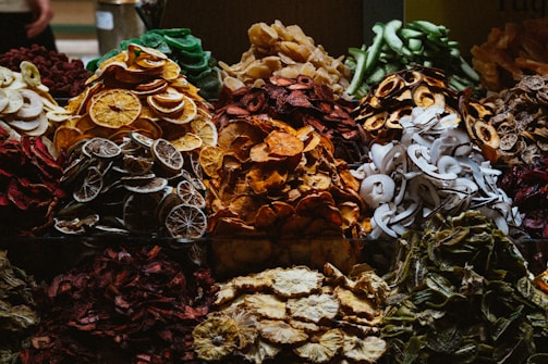 A variety of dried fruits are displayed in an arrangement, with distinct piles showcasing vibrant colors and textures. The assortment includes slices of oranges, apples, limes, and coconut, among others. The rich, organic hues create a visually appealing, rustic theme.