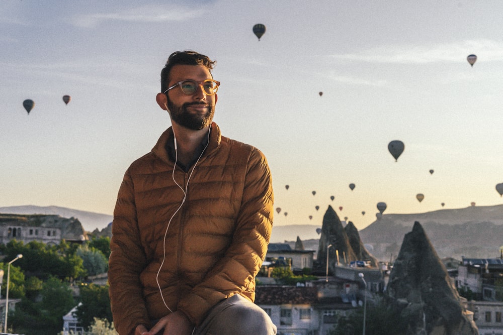 a man sitting on a ledge with many hot air balloons in the sky