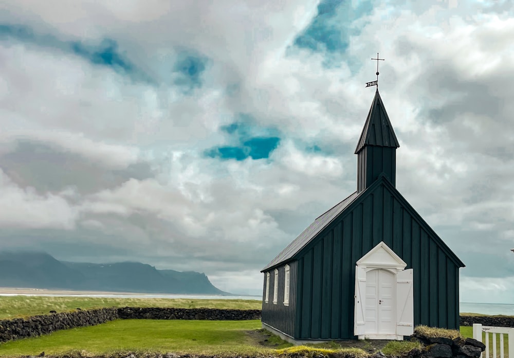 a small black church with a steeple on a cloudy day