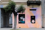 The storefront features a vibrant, colorful mural with bubble patterns painted in shades of pink, purple, and orange. Visible are a tree with lush green leaves, a sign with the number 55 on the wall, and a gate. The shop appears to be named 'Bubbles' with signage on a window and door.