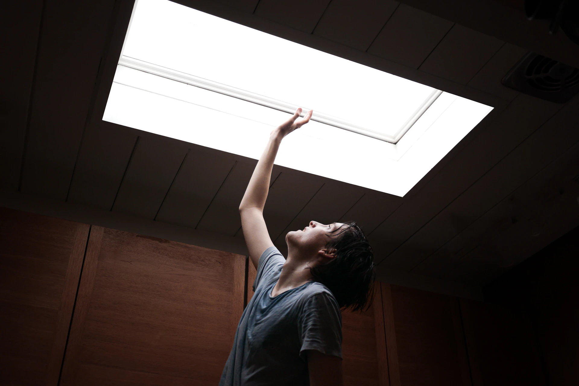 a woman reaching up to a skylight in a room