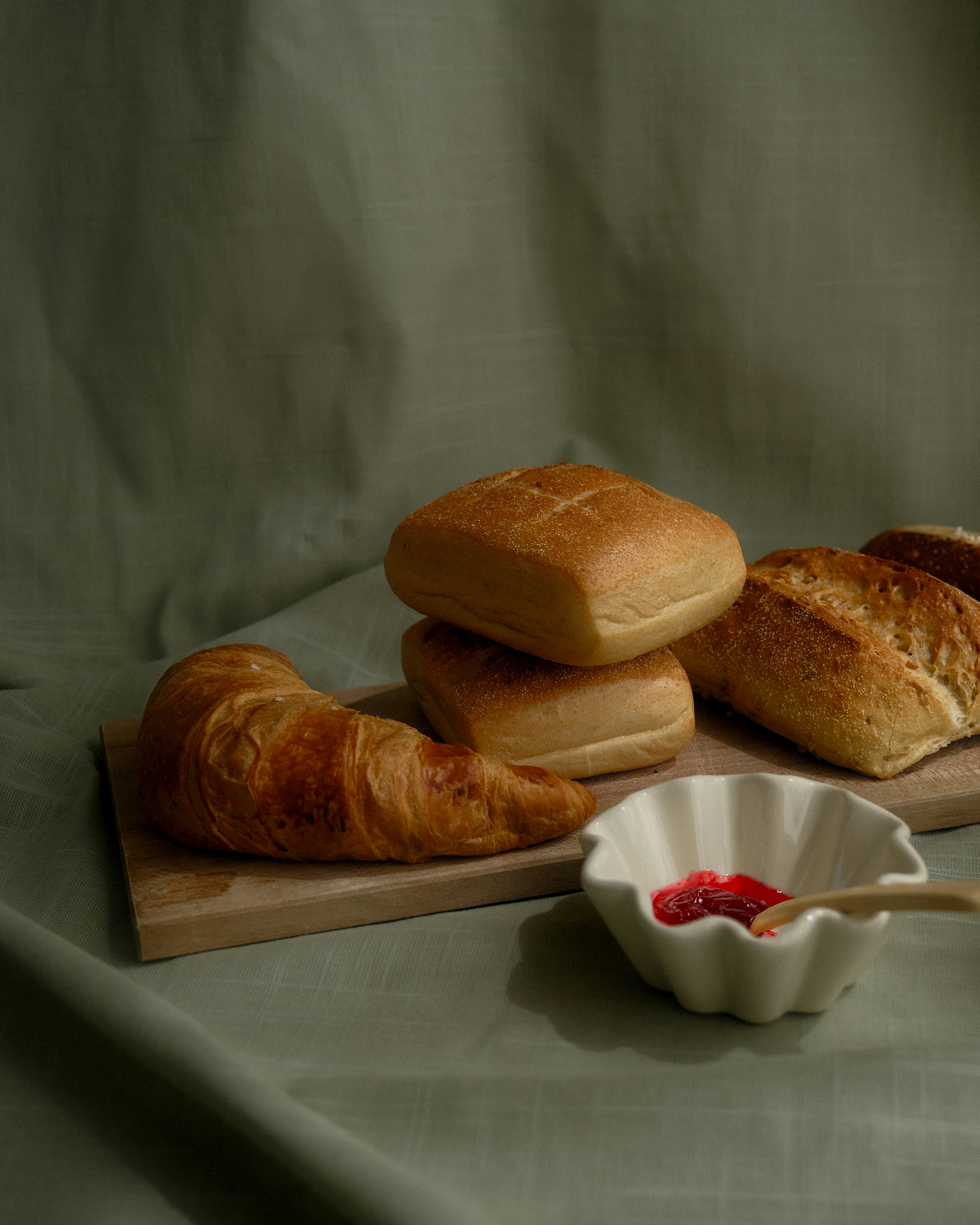 Pequeñas piezas de pan y facturas sobre una tabla y un pequeño recipiente de cerámica blanco con un poco de dulce de color rojo.