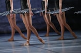 Ballet dancers in tutus are poised on stage, demonstrating graceful movements and coordination. The focus is on their legs, showing strength and elegance, as they balance on pointe shoes.