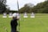 An individual is practicing archery in an open field with multiple targets set at varying distances. The person has a bow drawn back, aiming at the targets which feature traditional bullseye patterns. Surrounding the field are trees, creating a natural setting.