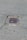 A metal drain cover is set into cracked asphalt pavement. Some small patches of grass are visible around the edges of the drain.