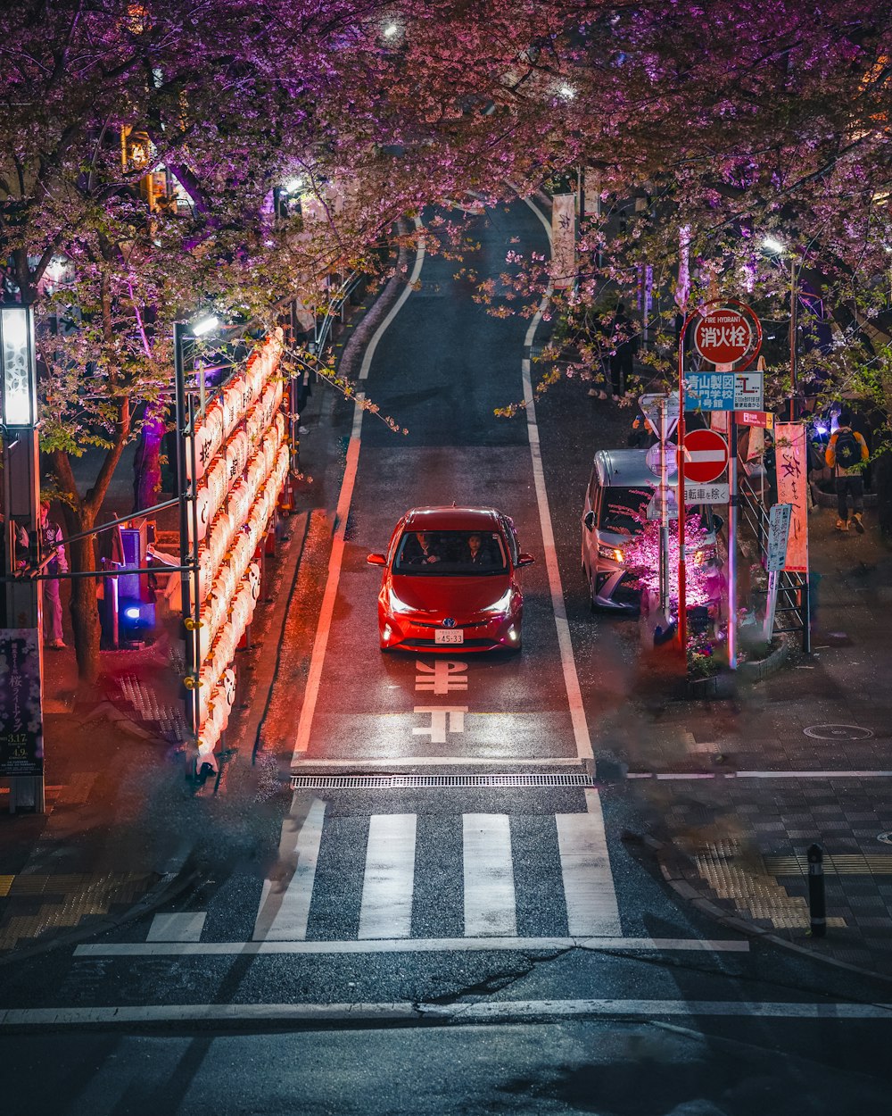 a red car driving down a street at night