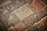 A textured surface composed of irregularly shaped stone tiles in various shades of brown, grey, and beige. The stones have a worn appearance with visible imperfections and some patina.
