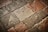 A textured surface composed of irregularly shaped stone tiles in various shades of brown, grey, and beige. The stones have a worn appearance with visible imperfections and some patina.