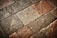A textured surface composed of irregularly shaped stone tiles in various shades of brown, grey, and beige. The stones have a worn appearance with visible imperfections and some patina.