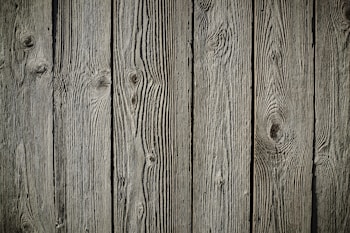 Wooden planks with a natural texture and prominent grain patterns, showcasing knots and aged characteristics, suggesting weathering and exposure.