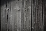 Weathered wooden planks are aligned vertically, showcasing a rustic and textured appearance with visible grain patterns and natural knots.