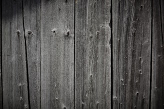 Weathered wooden planks are aligned vertically, showcasing a rustic and textured appearance with visible grain patterns and natural knots.