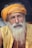 An elderly man with a long white beard and mustache wears a bright orange turban and yellow shirt, displaying a serene and contemplative expression. The background is dark, highlighting his facial features and attire.