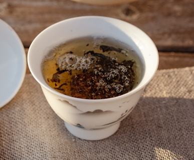 A teacup filled with tea leaves and tea water, with bubbles floating on the surface of the water