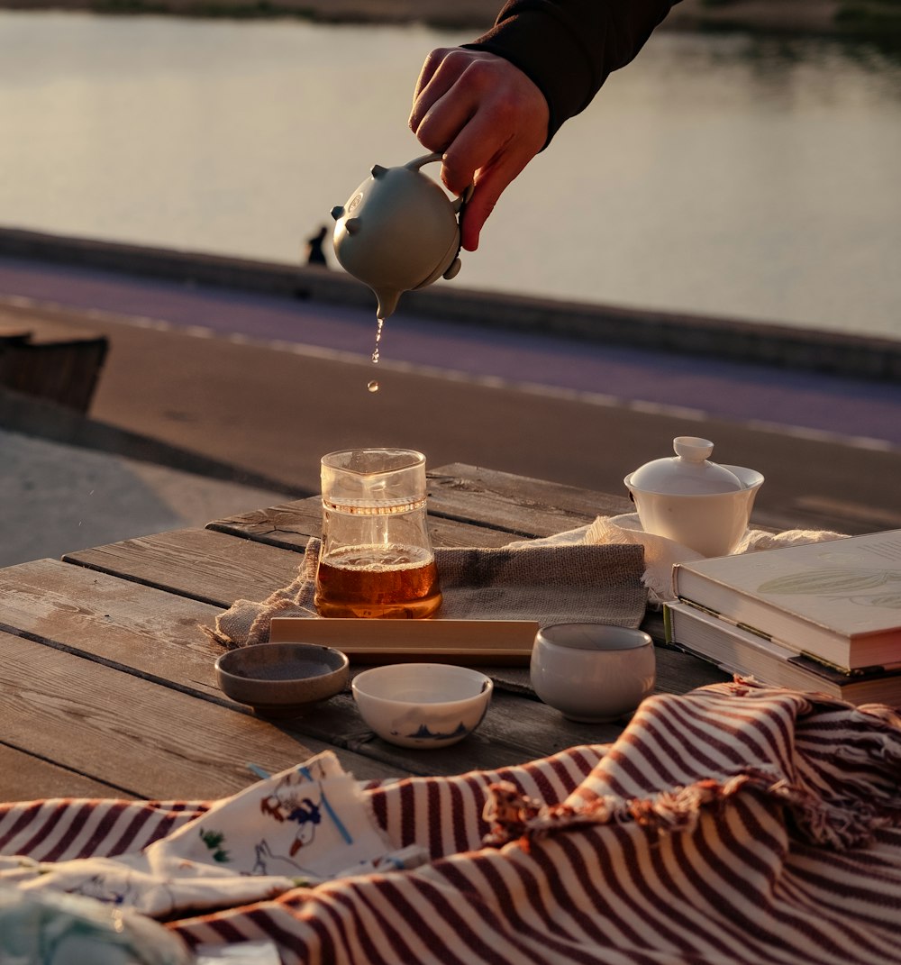 a person pouring tea into a cup on a picnic table