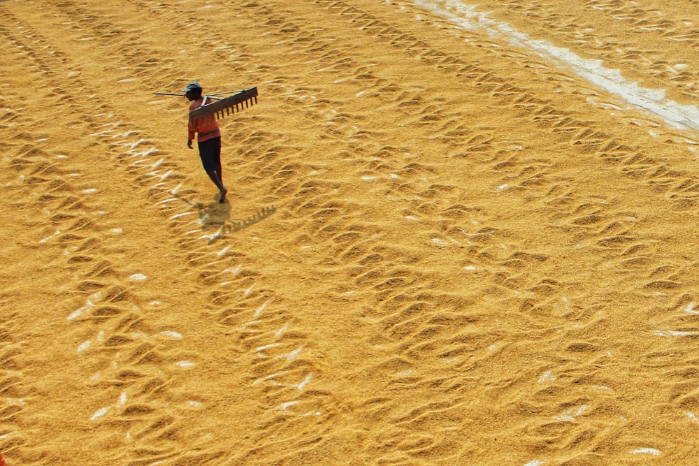 a man walking across a sandy beach holding a surfboard