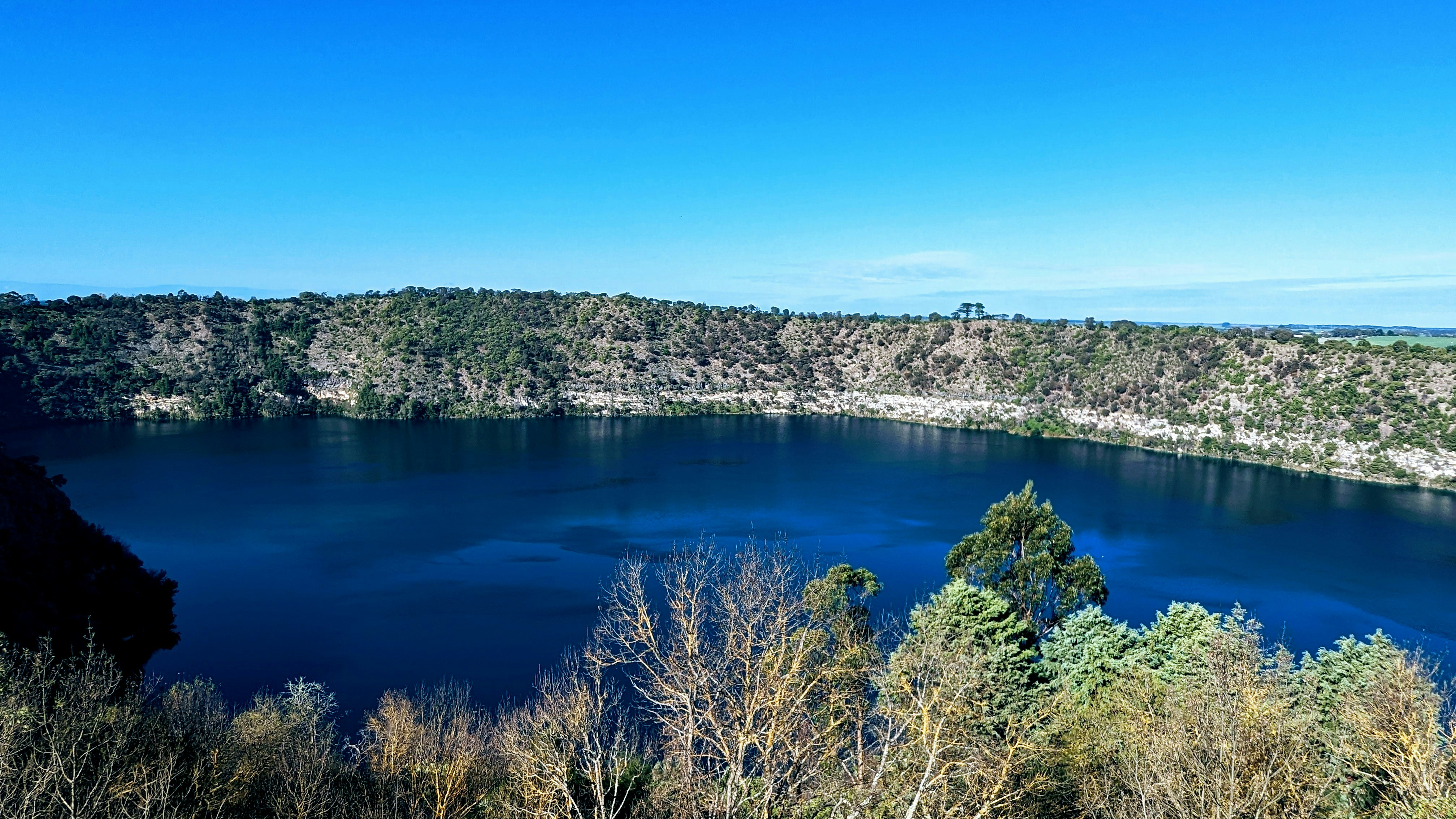 a blue lake surrounded by trees on a sunny day
