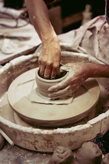 Artisans working together, shaping clay on a pottery wheel in a bright studio.