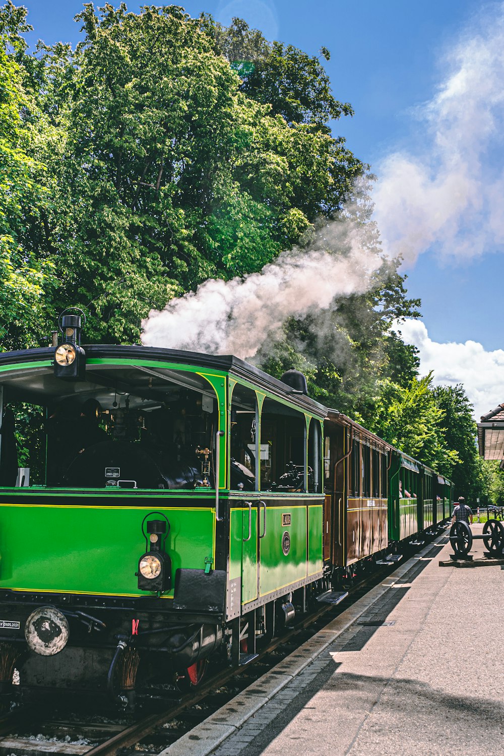 a green train traveling down train tracks next to a forest