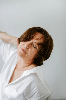 a woman in a white shirt is holding her hands behind her head