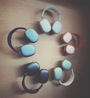 A collection of over-ear headphones in various colors forms a circular pattern against a wooden background. Each pair of headphones has a sleek modern design, shown in colors like red, blue, and cream.