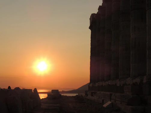 A dramatic sunset over the ancient ruins of a Seljuk caravanserai, with warm golden light illuminating the stone arches.