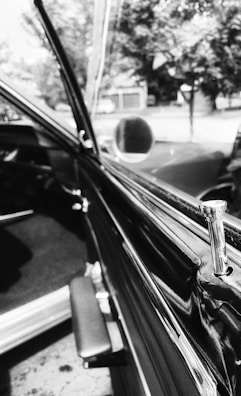 Close-up of a chauffeur’s hand opening a premium car door, in high-contrast black and white.