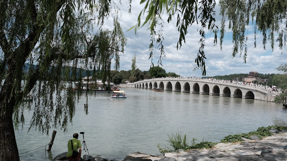 a man standing on the bank of a river next to a bridge