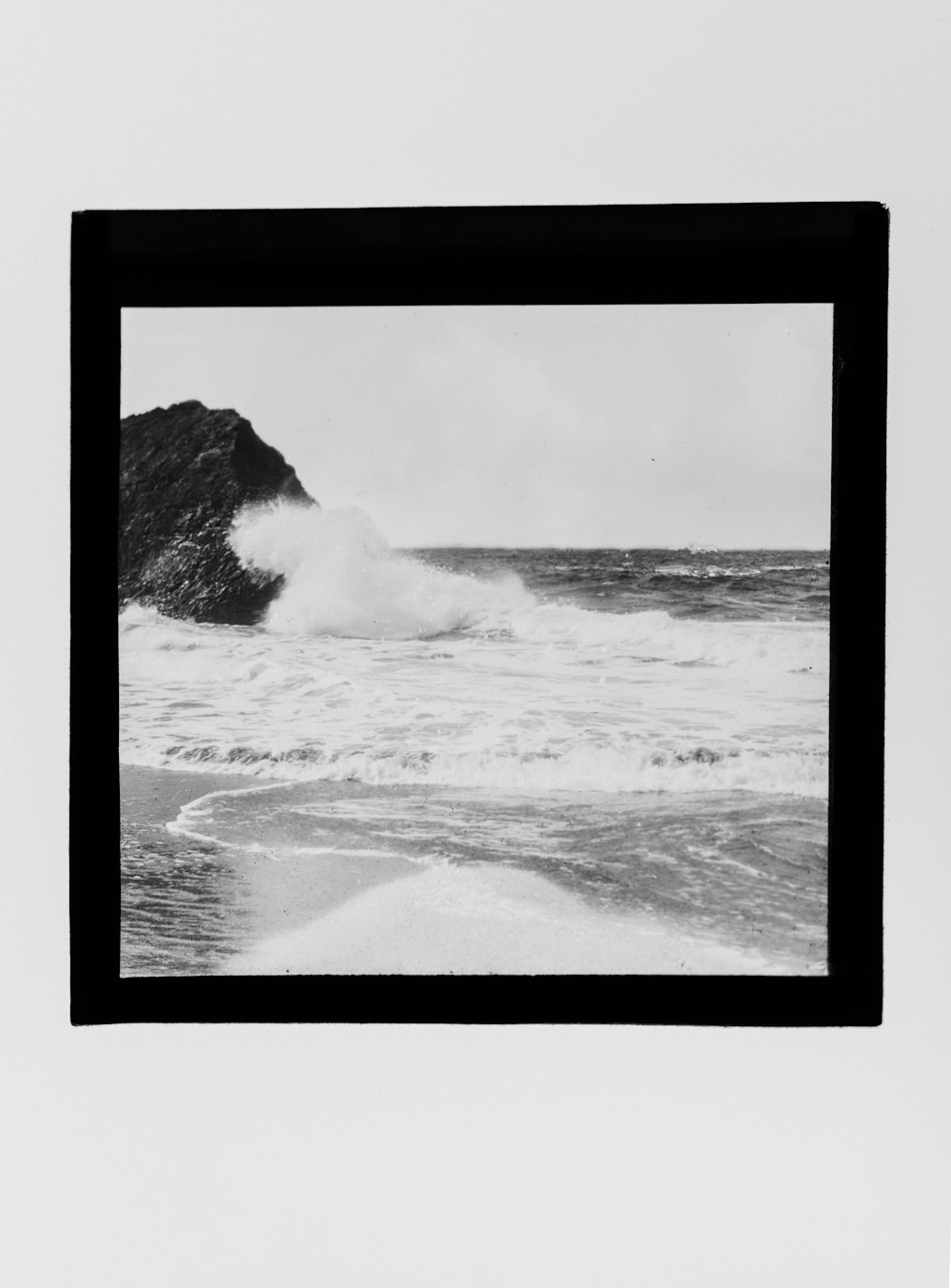 a black and white photo of a wave crashing on the beach