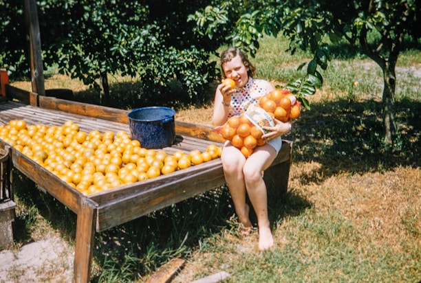 Smiling farmer holding a crate full of ripe oranges in a lush citrus grove.