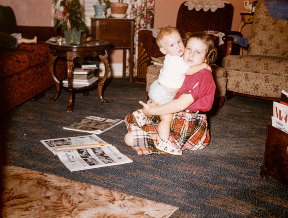 a young girl holding a baby while sitting on the floor