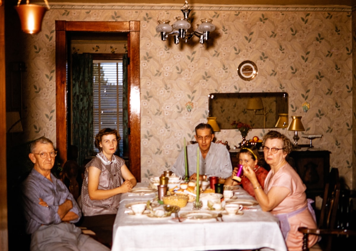 Family gathered around a dinner table in warm, film-grain light.