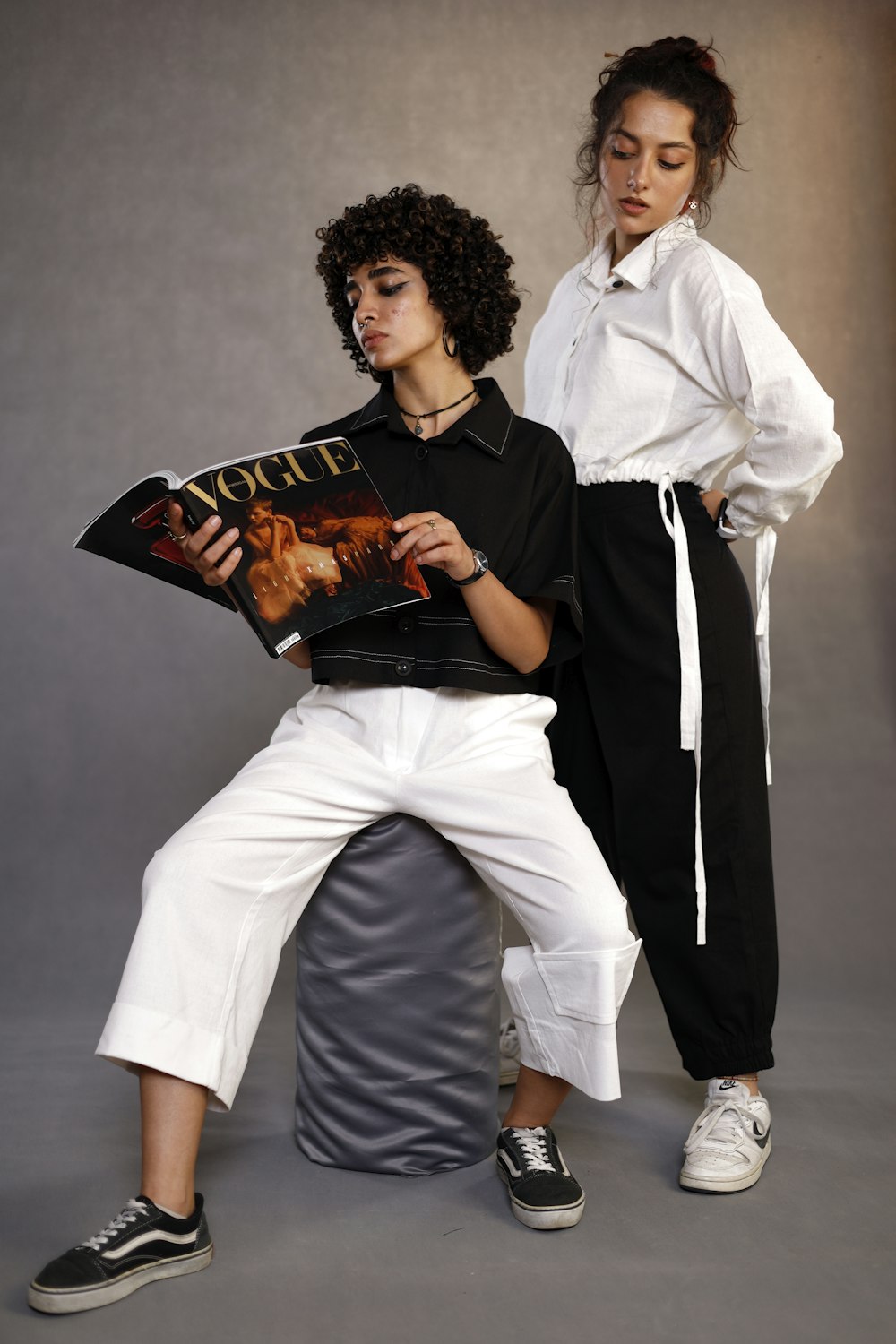 two young women sitting on a stool reading a magazine