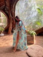 A model wearing a cozy, earth-toned traditional dress standing in a sunlit rustic room.