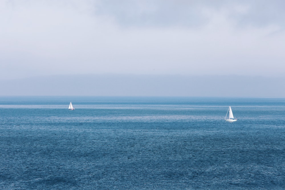 two sailboats in the ocean on a cloudy day