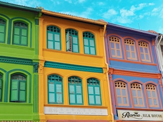 A vibrant building facade being repainted by skilled painters under bright daylight.