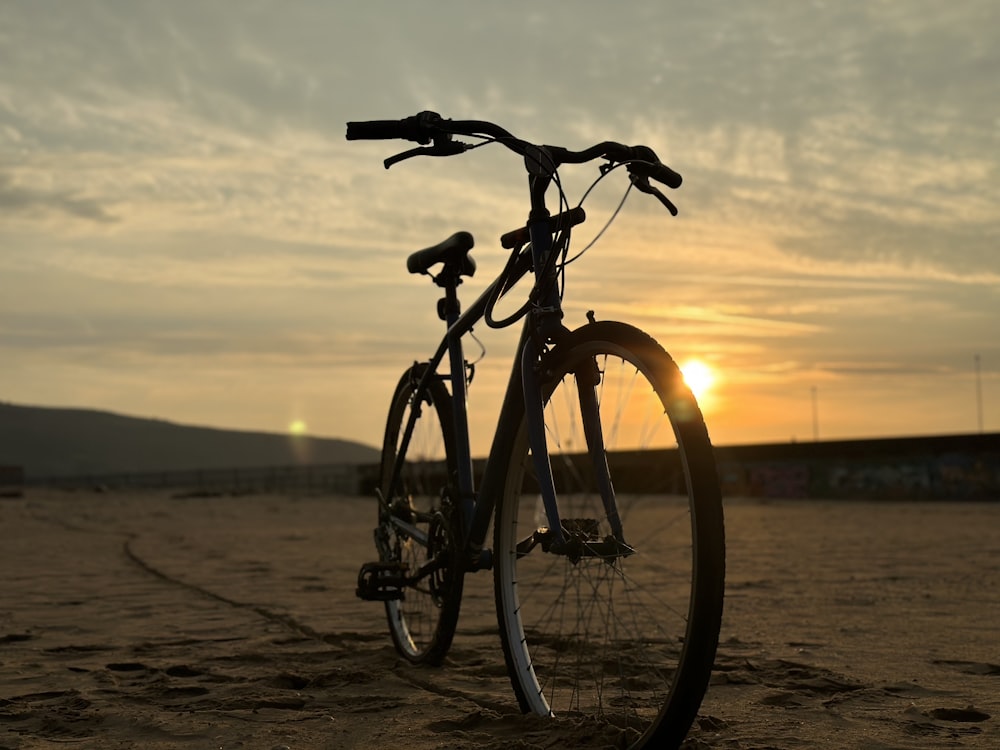 a bike parked on the beach at sunset