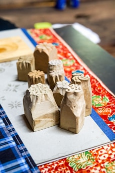 A close-up view of intricately carved wooden stamps with floral designs. These stamps are placed on a table covered with colorful fabric, displaying vibrant patterns such as floral and plaid prints.