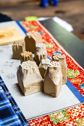 A close-up view of intricately carved wooden stamps with floral designs. These stamps are placed on a table covered with colorful fabric, displaying vibrant patterns such as floral and plaid prints.